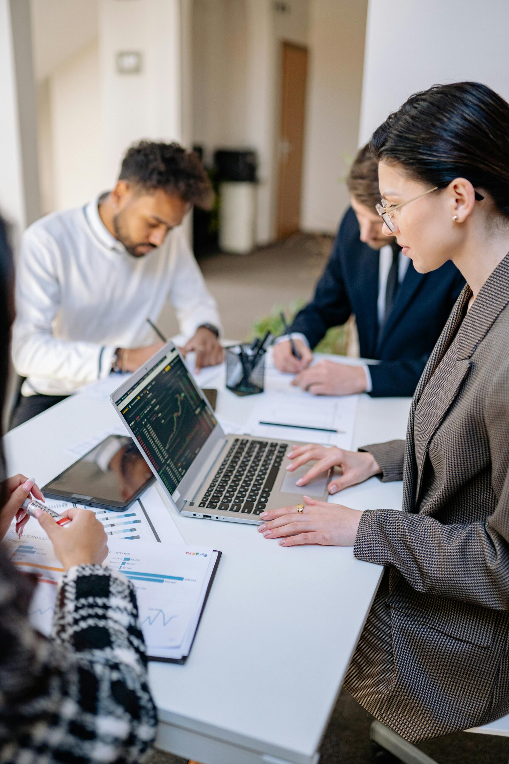 A group of professionals collaborating at a desk with laptops and paperwork.